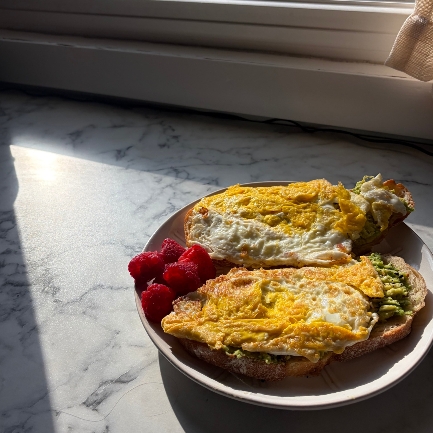 Avocado toast topped with eggs with a side of raspberries