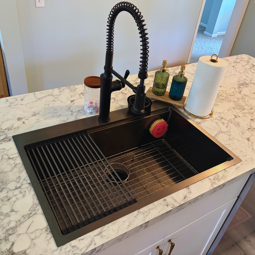 Kitchen sink with drying rack set up on the left side of the sink. Two soap dispensers, paper towel roll, and candy jar are set up alongside the sink.
