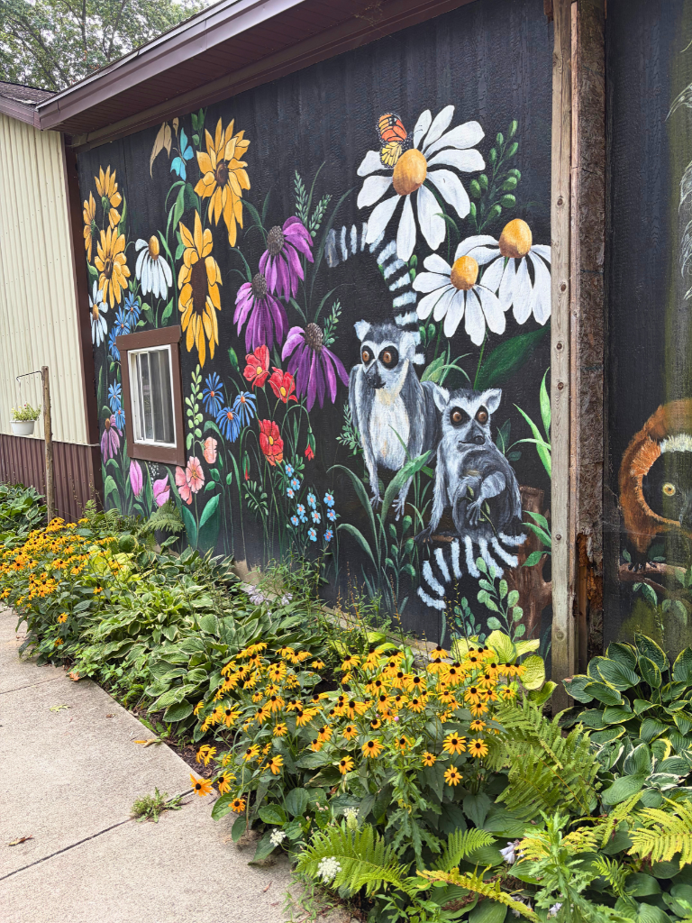 Mural of lemurs and flowers with flowers and landscaping sitting in front of the wall