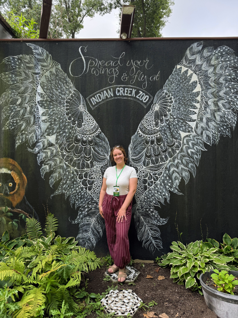 Kait standing in front of a mural of wings at the zoo